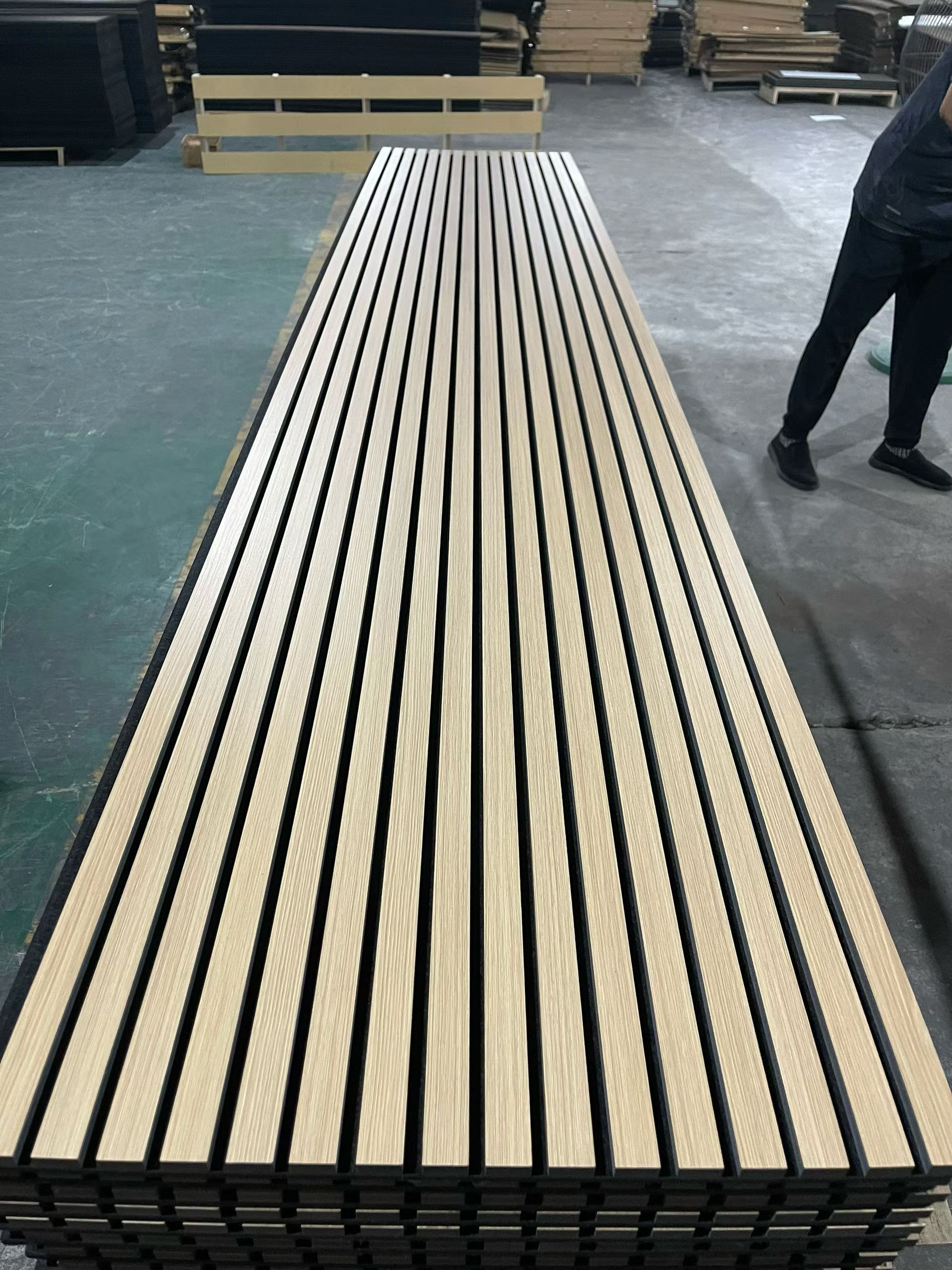 Stack of acoustic slat panels in factory - light wood slats on black PET backing